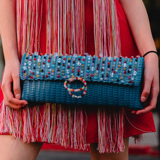 Woman in a red dress with fringe holding a blue bag in an urban setting